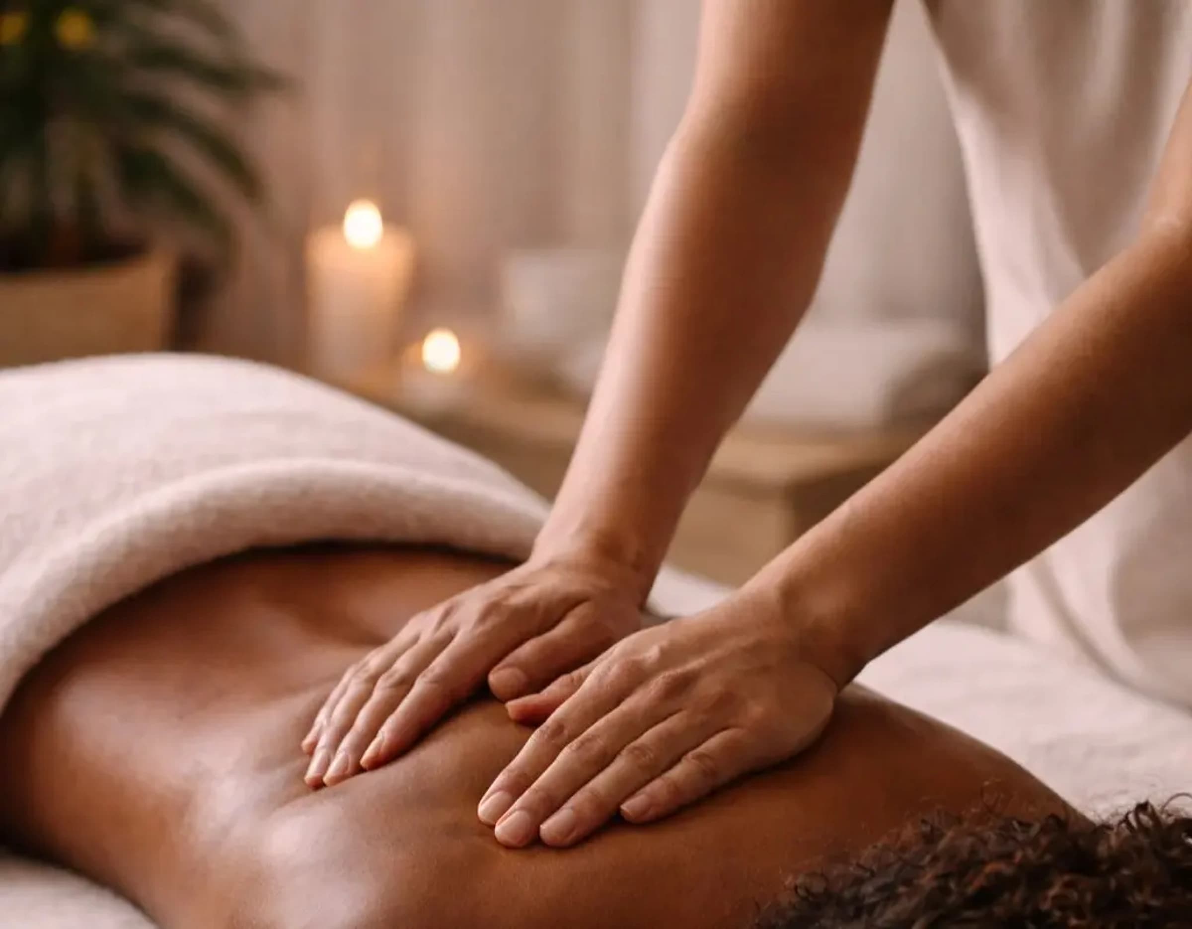 Massage therapist's hands on a client's back in a warm, softly lit spa with candles and folded towels.